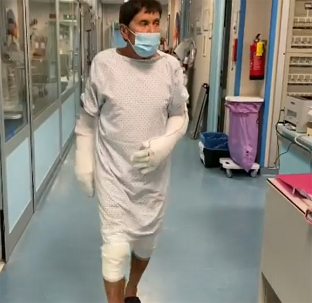 Gianni con le braccia completamente fasciate e parte delle gambe bendate, cammina nel corridoio dell'ospedale